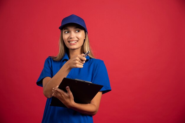 Mulher sorridente de uniforme azul, posando com prancheta e lápis.