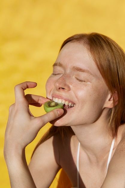 Mulher sorridente de vista lateral comendo kiwi