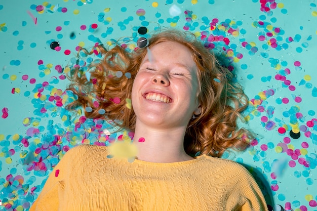 Mulher sorridente deitada no chão com confetes ao redor