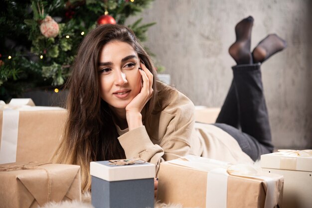 Mulher sorridente deitada no tapete fofo com presentes de Natal.