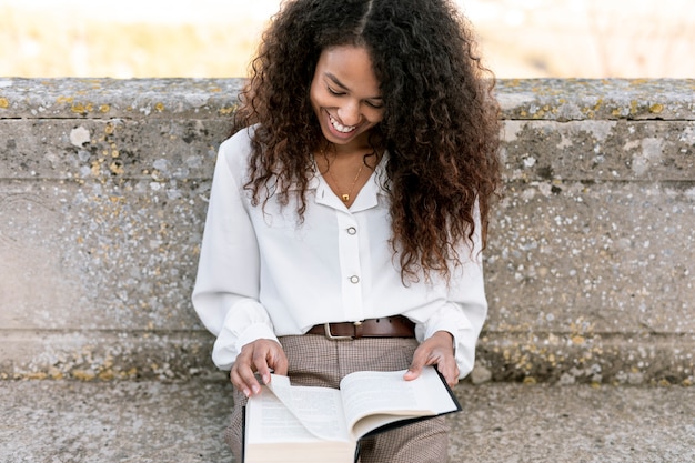 Mulher sorridente, desfrutando de um livro ao ar livre