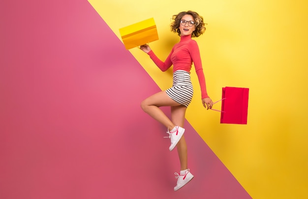 Foto grátis mulher sorridente e atraente com roupa colorida elegante pulando com sacolas de compras