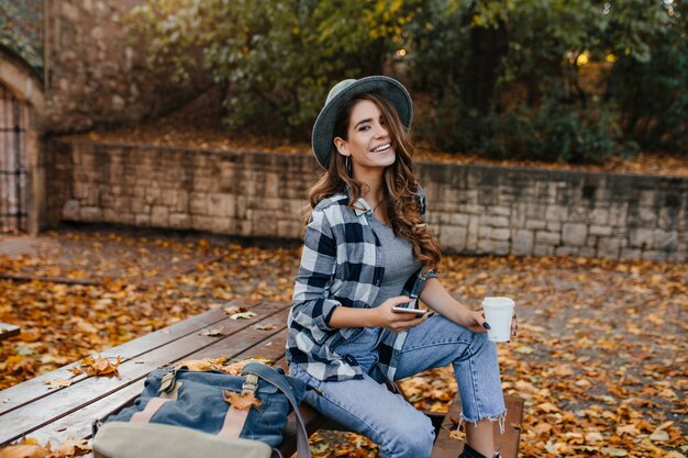 Mulher sorridente e bem vestida com cabelo castanho-claro sentada no parque no dia de outubro apreciando a vista da natureza