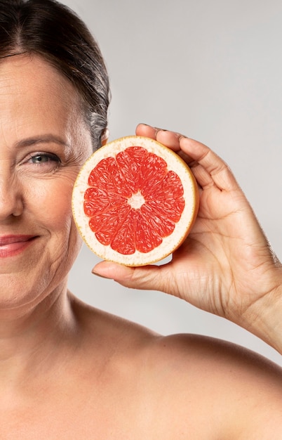 Mulher sorridente e idosa segurando metade de uma toranja