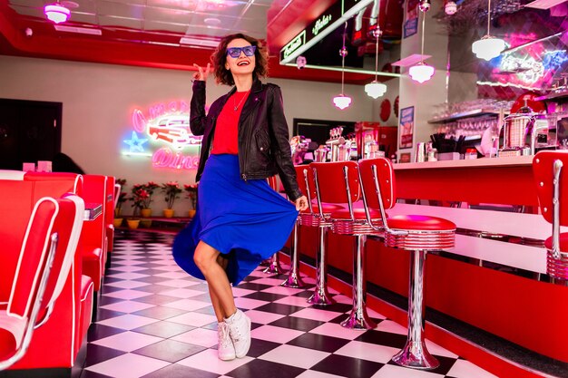 Mulher sorridente elegante em roupa colorida em um café retrô vintage dos anos 50 dançando