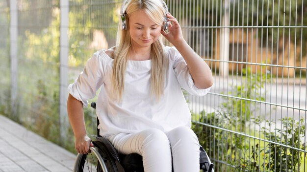 Mulher sorridente em cadeira de rodas com fones de ouvido do lado de fora