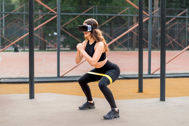 Foto grátis mulher sorridente em fone de ouvido vr em um agasalho fazendo exercícios com elástico em um campo esportivo