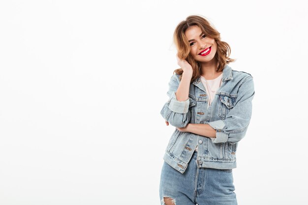 Mulher sorridente em roupas jeans posando sobre parede branca