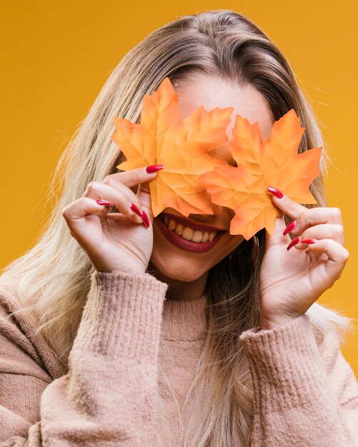 Mulher sorridente, escondendo, dela, olhos, com, maple sai, contra, fundo amarelo