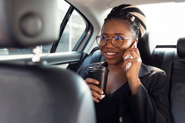 Mulher sorridente falando ao telefone no banco de trás do carro enquanto toma café