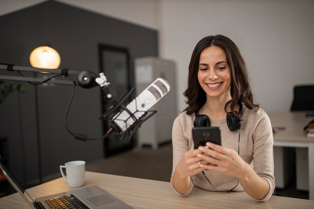 Mulher sorridente fazendo um podcast no rádio com um microfone e um smartphone