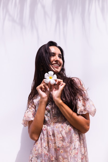 Mulher sorridente feliz de cabelos compridos em um vestido fica na parede branca