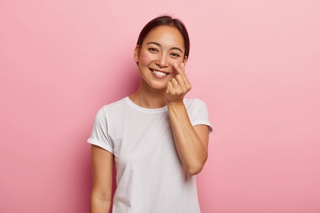 Mulher sorridente fofa toca pele ruge nas bochechas com o dedo, demonstra sua suavidade, se preocupa com sua beleza, inclina a cabeça, sorri gentilmente, vestida com camiseta branca casual, modelos internos