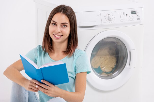 Mulher sorridente, lendo perto de máquina de lavar roupa