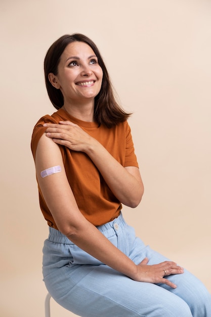 Mulher sorridente mostrando adesivo no braço após tomar vacina