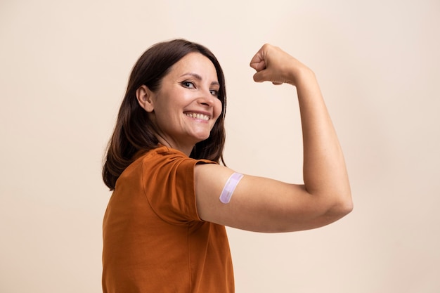 Mulher sorridente mostrando adesivo no braço após tomar vacina