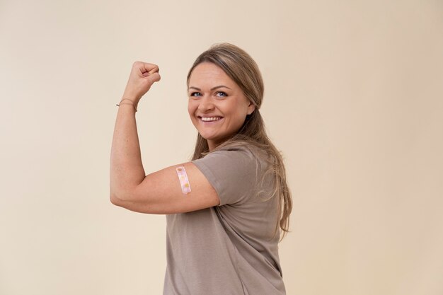 Mulher sorridente mostrando bíceps com adesivo após tomar vacina