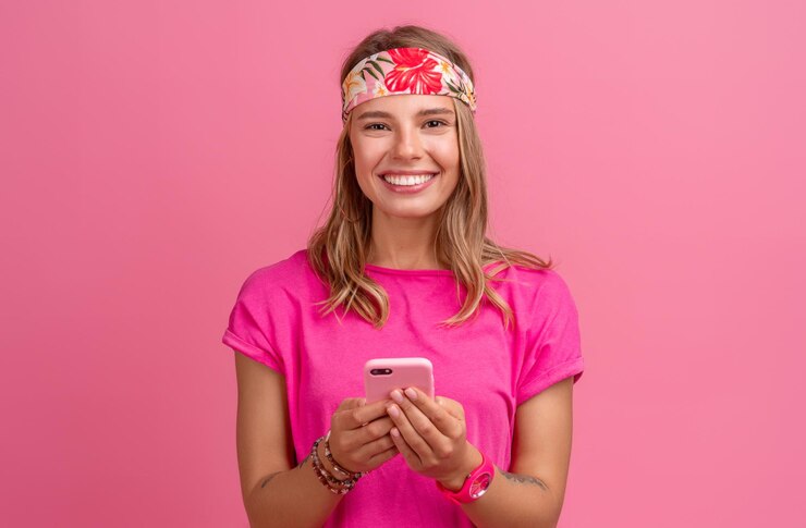 Foto grátis mulher sorridente muito fofa em acessórios de estilo hippie boho de camisa rosa sorrindo diversão emocional posando em fundo rosa isolado humor positivo usando smartphone