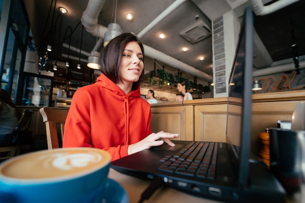 Mulher sorridente no bar tomando um café e usando um laptop