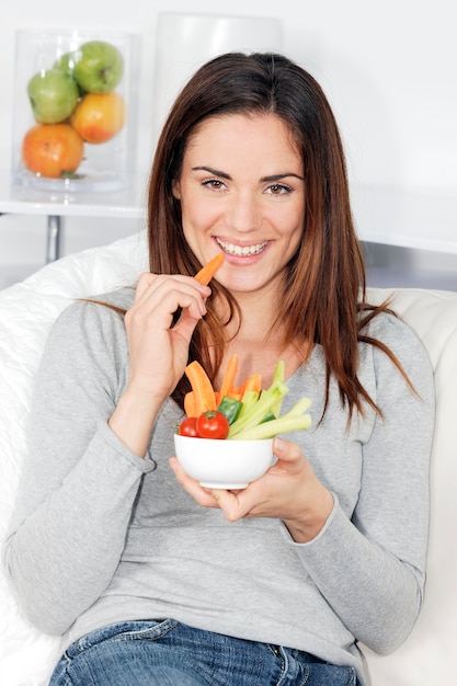 Mulher sorridente no sofá com salada de legumes