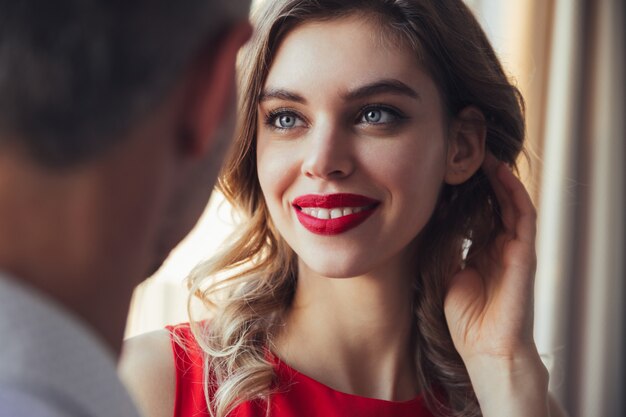 Mulher sorridente no vestido vermelho e com lábios vermelhos, olhando para o homem