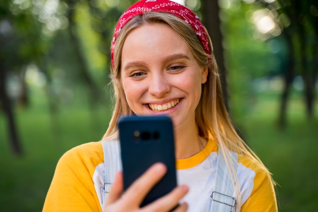 Mulher sorridente, olhando para o smartphone ao ar livre