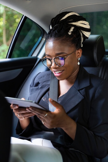 Mulher sorridente olhando para o tablet no banco de trás do carro