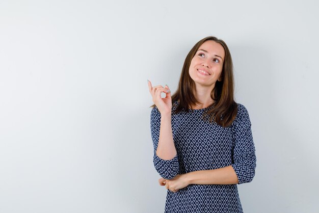 Mulher sorridente, olhando para o topo e apontando algo com os dedos no fundo branco