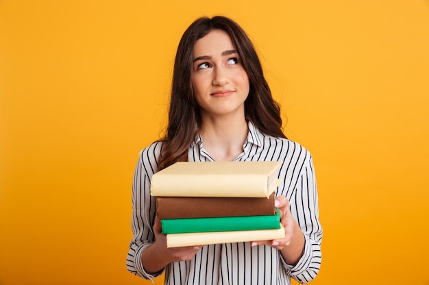 Mulher sorridente pensativa em camisa segurando livros e olhando para cima