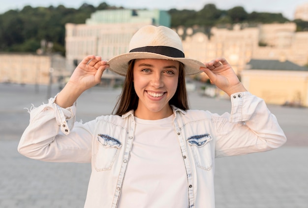 Mulher sorridente posando ao ar livre com chapéu enquanto viaja