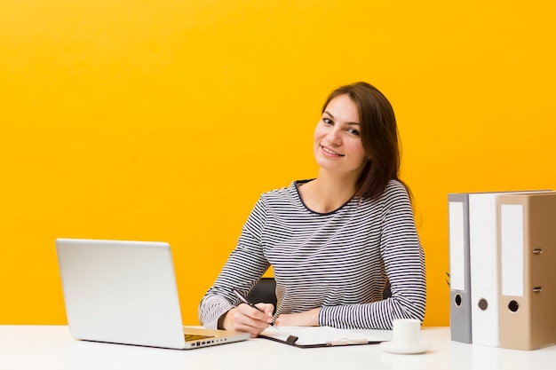 Mulher sorridente posando em sua mesa enquanto escrevia algo