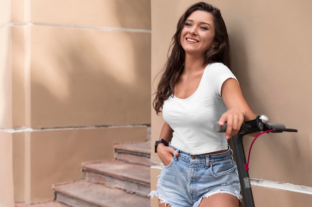 Mulher sorridente posando enquanto se inclina sobre uma scooter elétrica