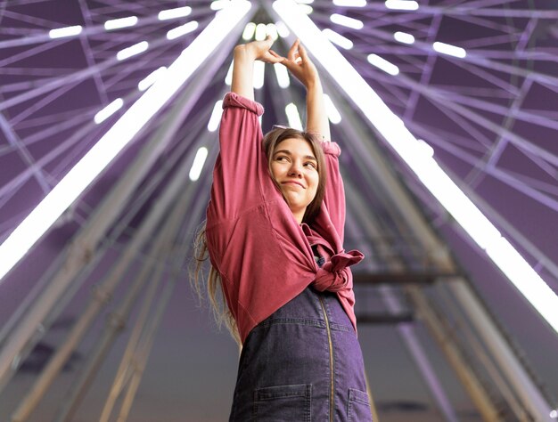 Mulher sorridente posando no parque de diversões ao lado da roda gigante