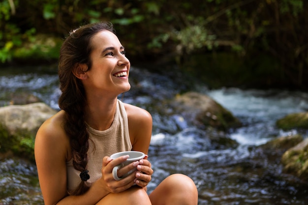 Mulher sorridente relaxando com uma caneca na natureza