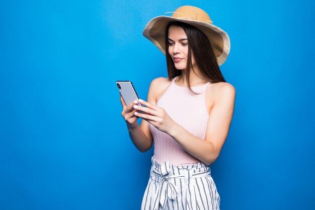 Mulher sorridente satisfeita digitando mensagem de texto ou percorrendo redes sociais usando smartphone isolado sobre a parede azul.