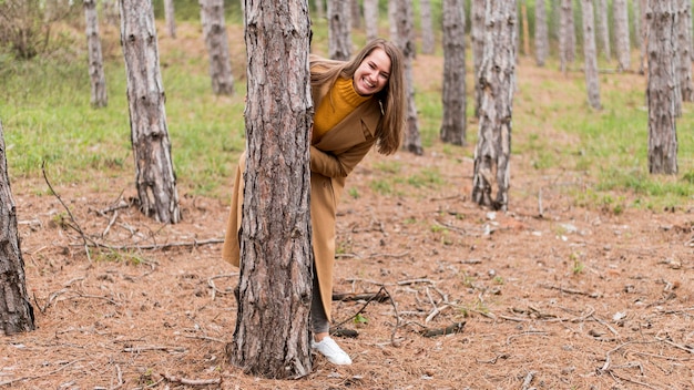 Mulher sorridente, se escondendo atrás de uma árvore