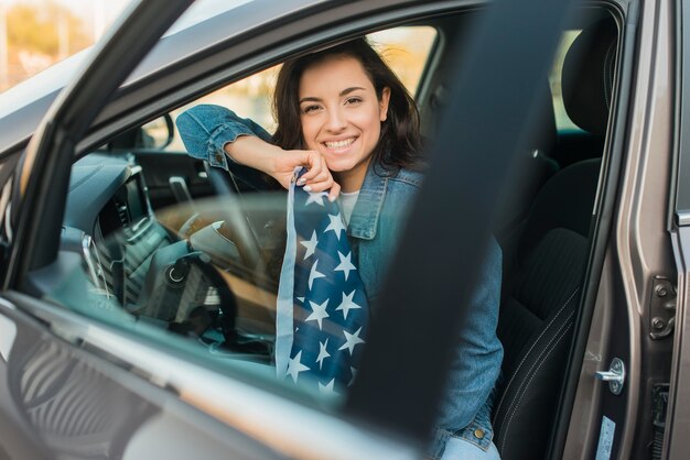 Mulher sorridente segurando a bandeira dos EUA grande no carro