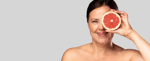 Mulher sorridente segurando metade da grapefruit sobre o rosto com espaço de cópia