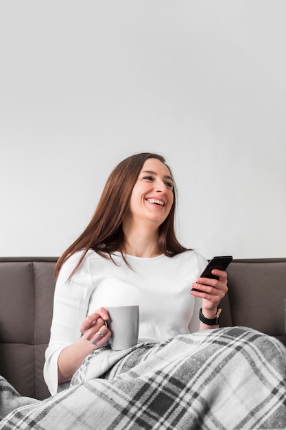 Mulher sorridente segurando smartphone e caneca