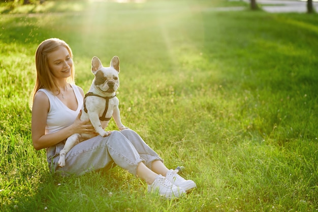 Mulher sorridente segurando um buldogue francês na grama