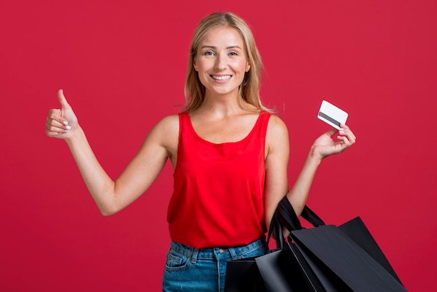 Mulher sorridente segurando um cartão de crédito e sacolas de compras enquanto faz sinal de positivo