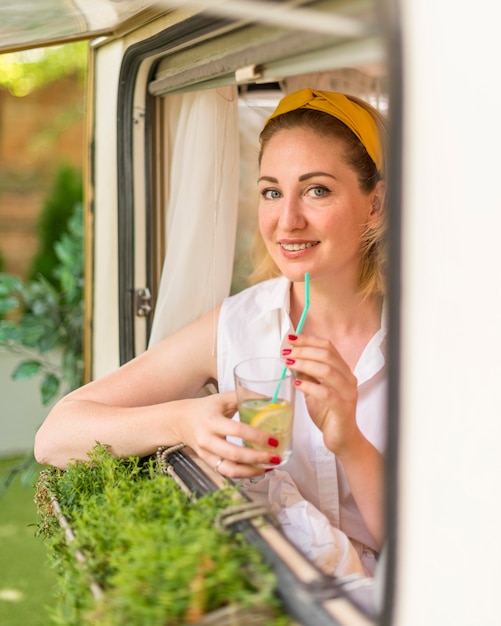 Mulher sorridente segurando um copo de limonada ao lado de uma caravana