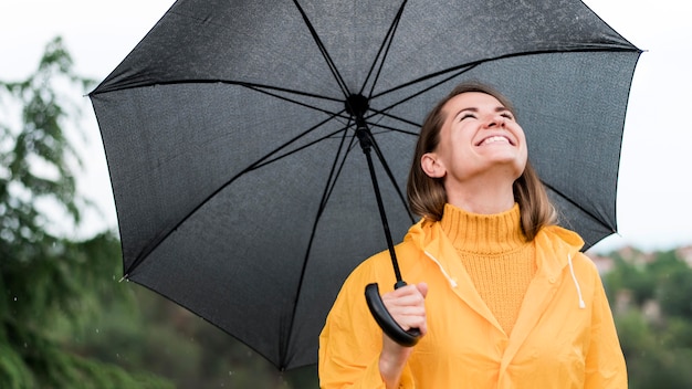 Mulher sorridente segurando um guarda-chuva preto aberto