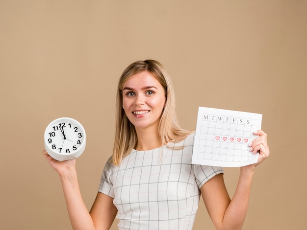 Mulher sorridente segurando um relógio e seu calendário de período