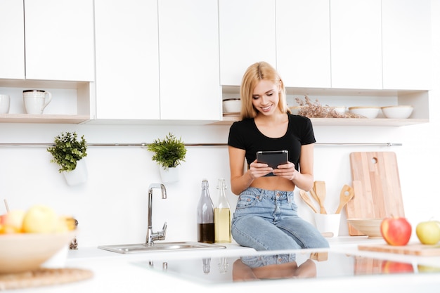 Mulher sorridente, sentado na mesa e usando tablet