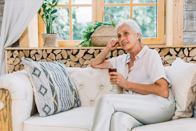 Mulher sorridente, sentar sofá, com, cruzado, perna, copo segurando, de, álcool