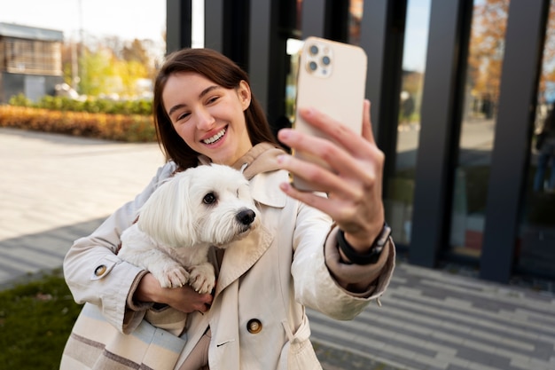 Mulher sorridente tirando selfie com cachorro plano médio