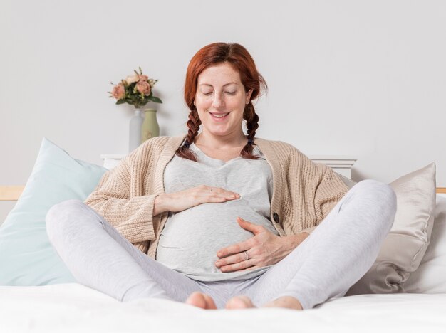 Mulher sorridente, tocando sua barriga de grávida