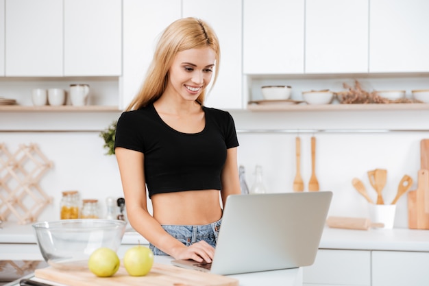 Mulher sorridente usando laptop na cozinha