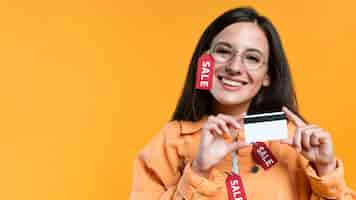 Foto grátis mulher sorridente usando óculos e jaqueta com etiqueta de venda e segurando um cartão de crédito